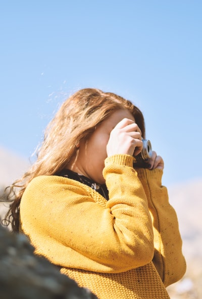 During the day wearing a brown sweater with a black and white camera woman
